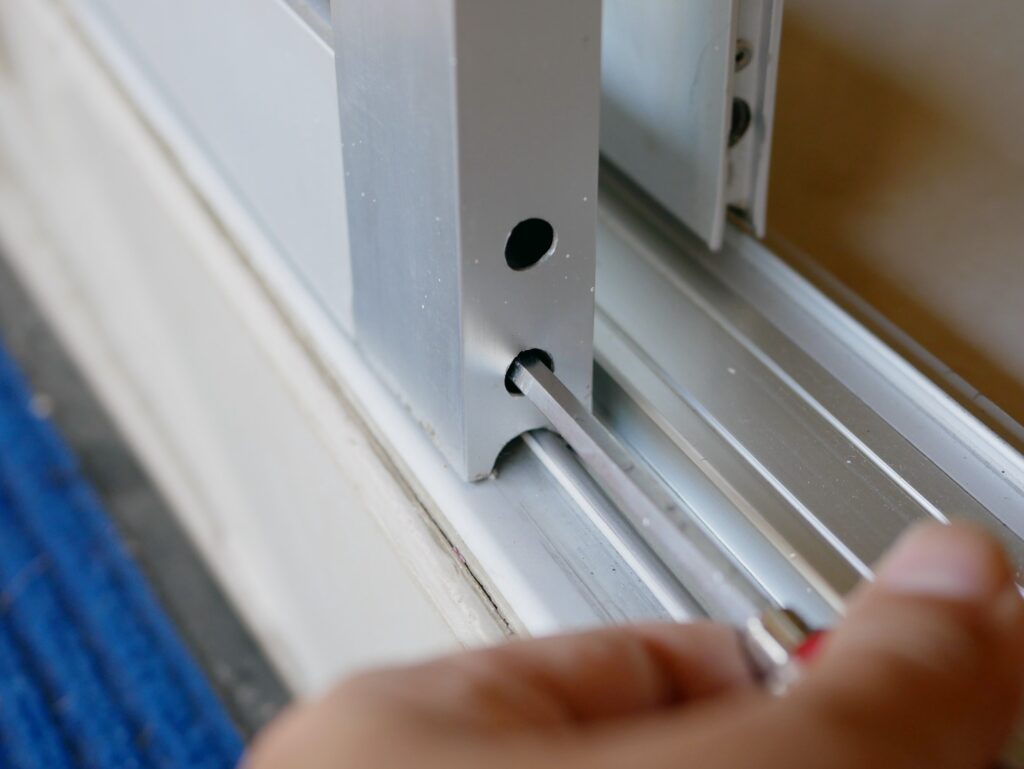 close up of a screwdriver in a man s hand adjusting sliding glass door rollers