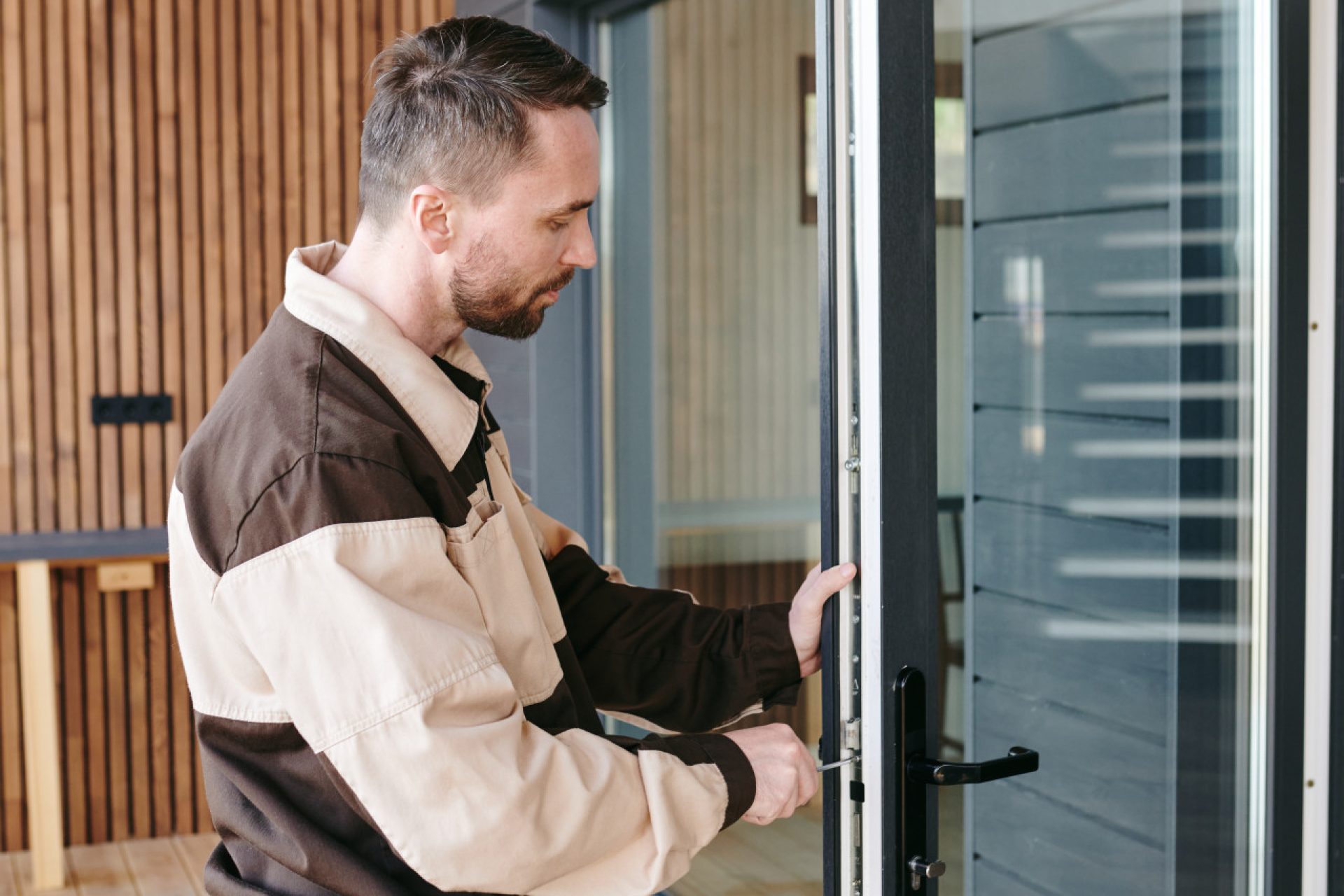 young-repairman-standing-front-glass-door-while-repairing-lock